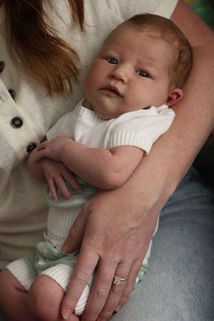 Close-up details of gentle hands and a white onesie in an indoor setting.