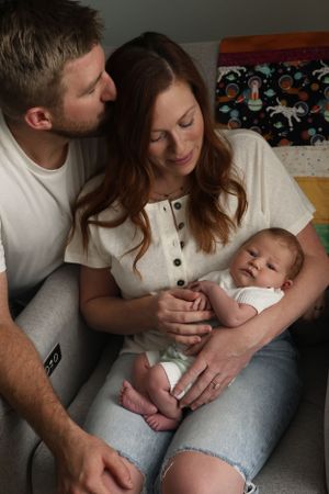 A tender family moment shared on a grey couch in natural lighting.