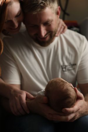 A tender moment showing a parent cradling a newborn baby in a white t-shirt.