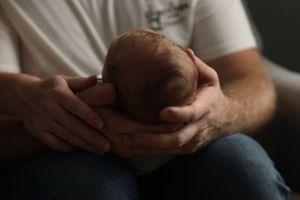 Parent in white shirt gently holding and looking down at sleeping newborn.