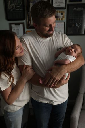 Parents share an intimate moment with their newborn baby against a wall with framed artwork.