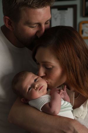 Intimate family moment with parents embracing their newborn baby in low light.