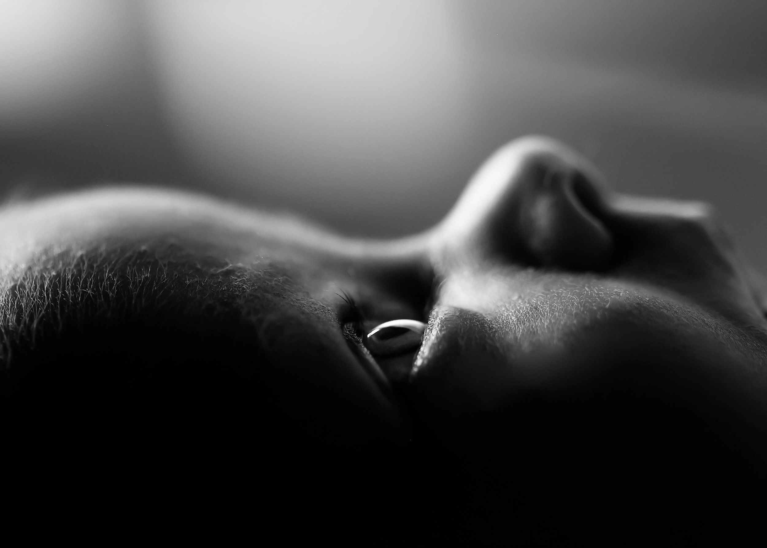 Close-up black and white portrait of a person lying down with a nose ring, soft bokeh background.