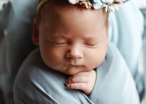 Peaceful newborn baby girl sleeping wrapped in a soft blue swaddle, wearing a delicate floral headband.