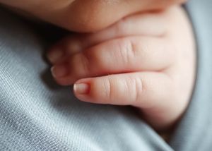 Close-up of a newborn baby's tiny delicate fingers and hand resting gently on a soft gray fabric.
