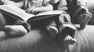 Black and white photo of children sitting on a couch reading a book together, with bare feet visible.