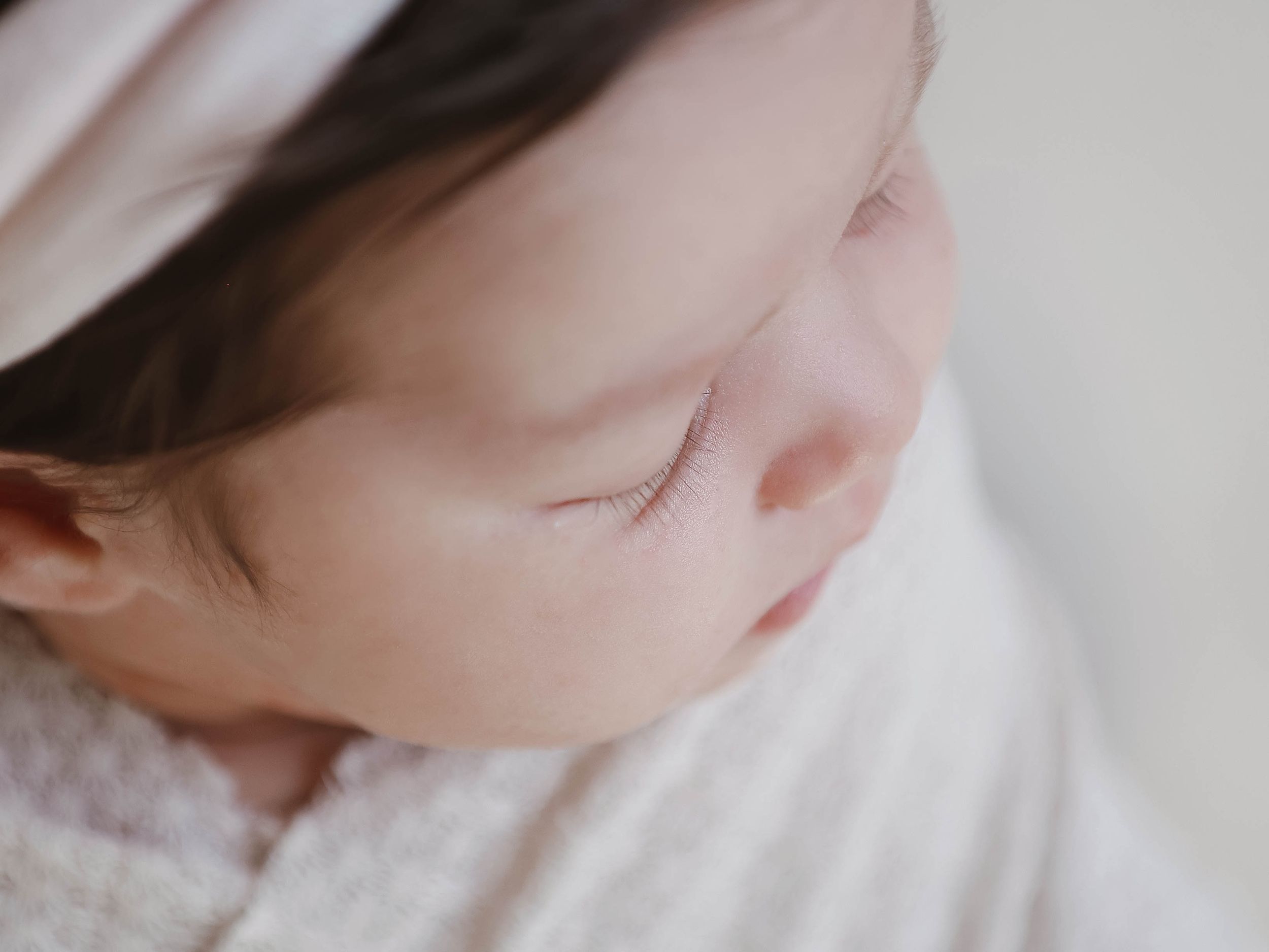 A sleeping baby photographed in soft lighting with white bedding.