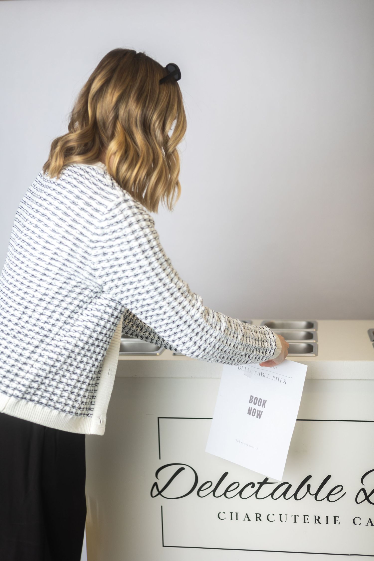 Someone in a patterned sweater reaching into a white box labeled Delectable Charcuterie.