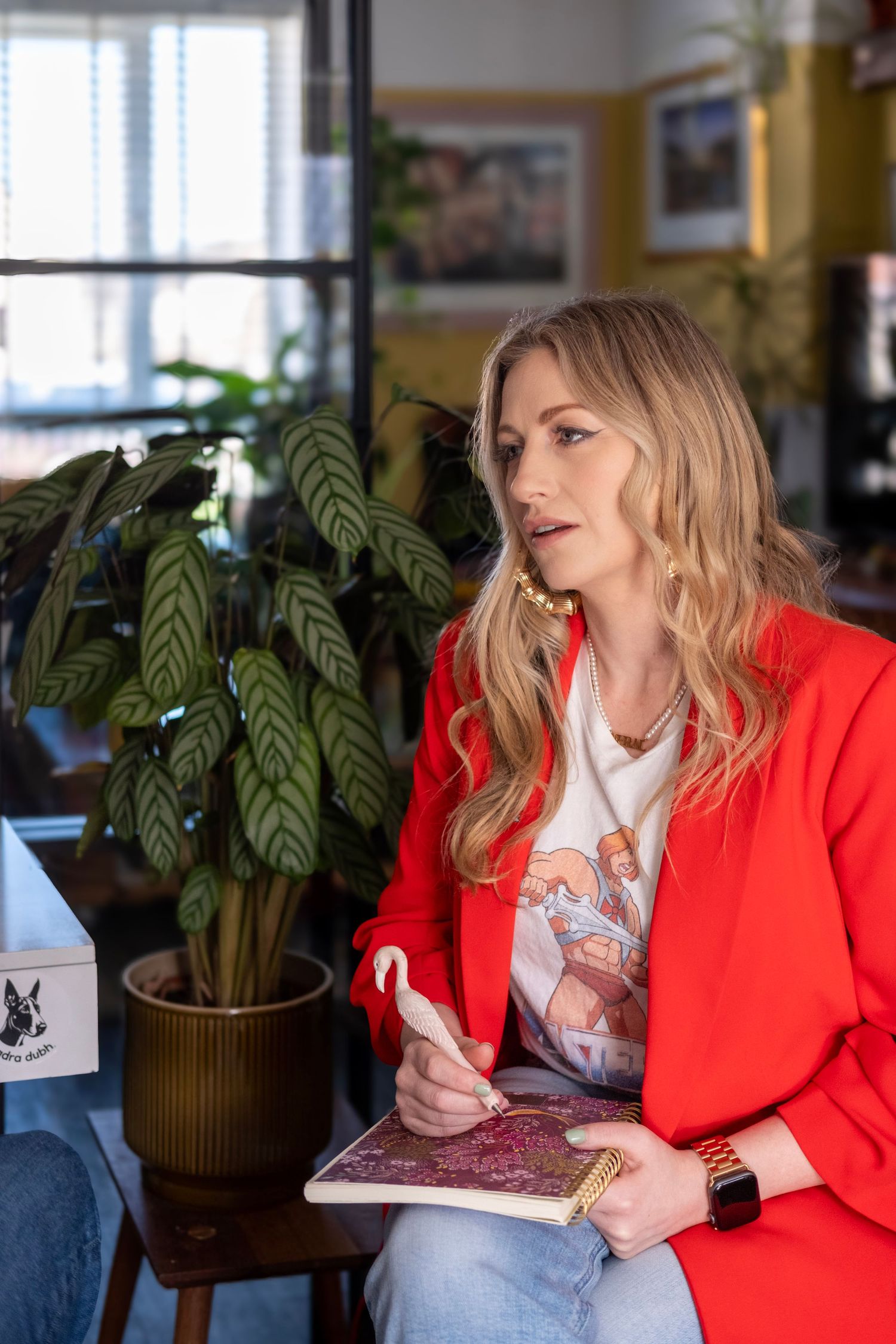 Woman in red blazer sitting with journal near houseplant.