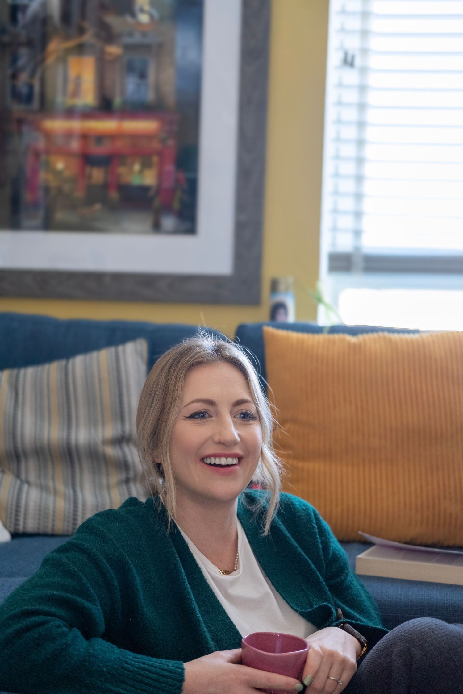 Woman relaxes on couch with coffee mug wearing green cardigan in cozy home setting.