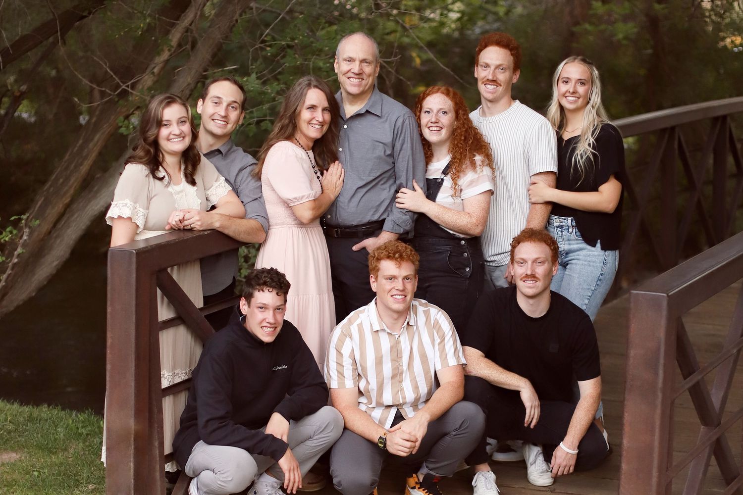 A group poses together on wooden stairs outdoors wearing coordinated light and dark clothing for a family portrait.