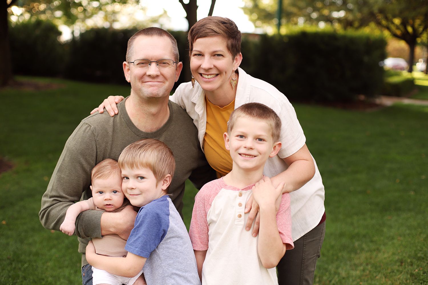 Family group enjoying a warm autumn day together in a park setting with sunlit trees in the background.