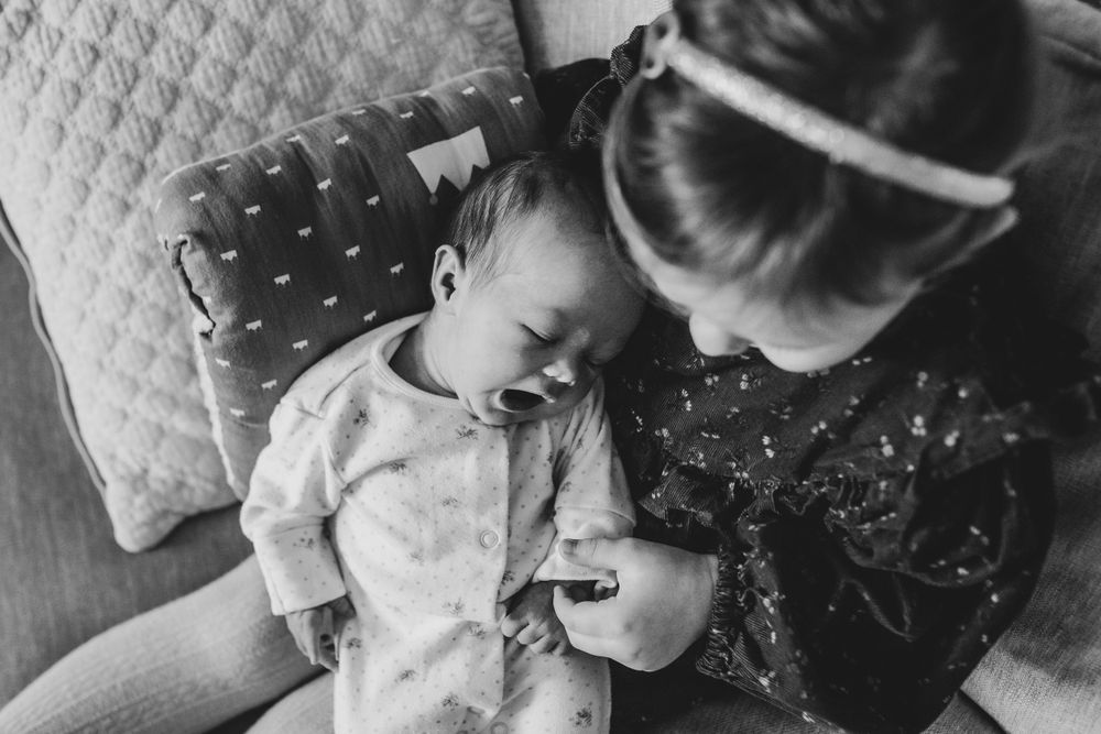 Black and white photograph showing a tender moment between caregiver and infant resting on a soft patterned couch.