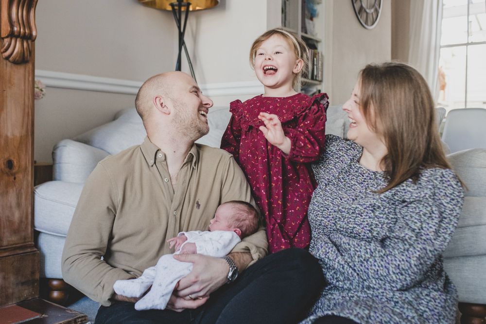 A joyful family moment in a living room with a small newborn and laughter shared on a couch.