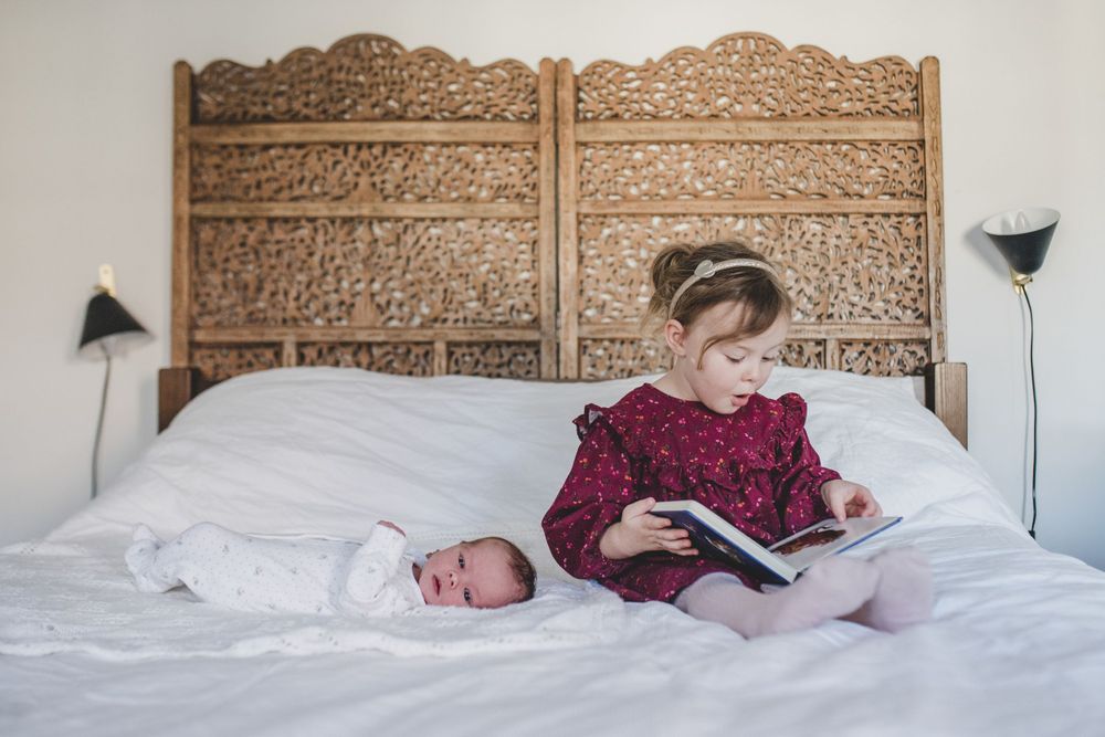 Two people relax on white bedding against an ornate carved wooden headboard while reading a book together.