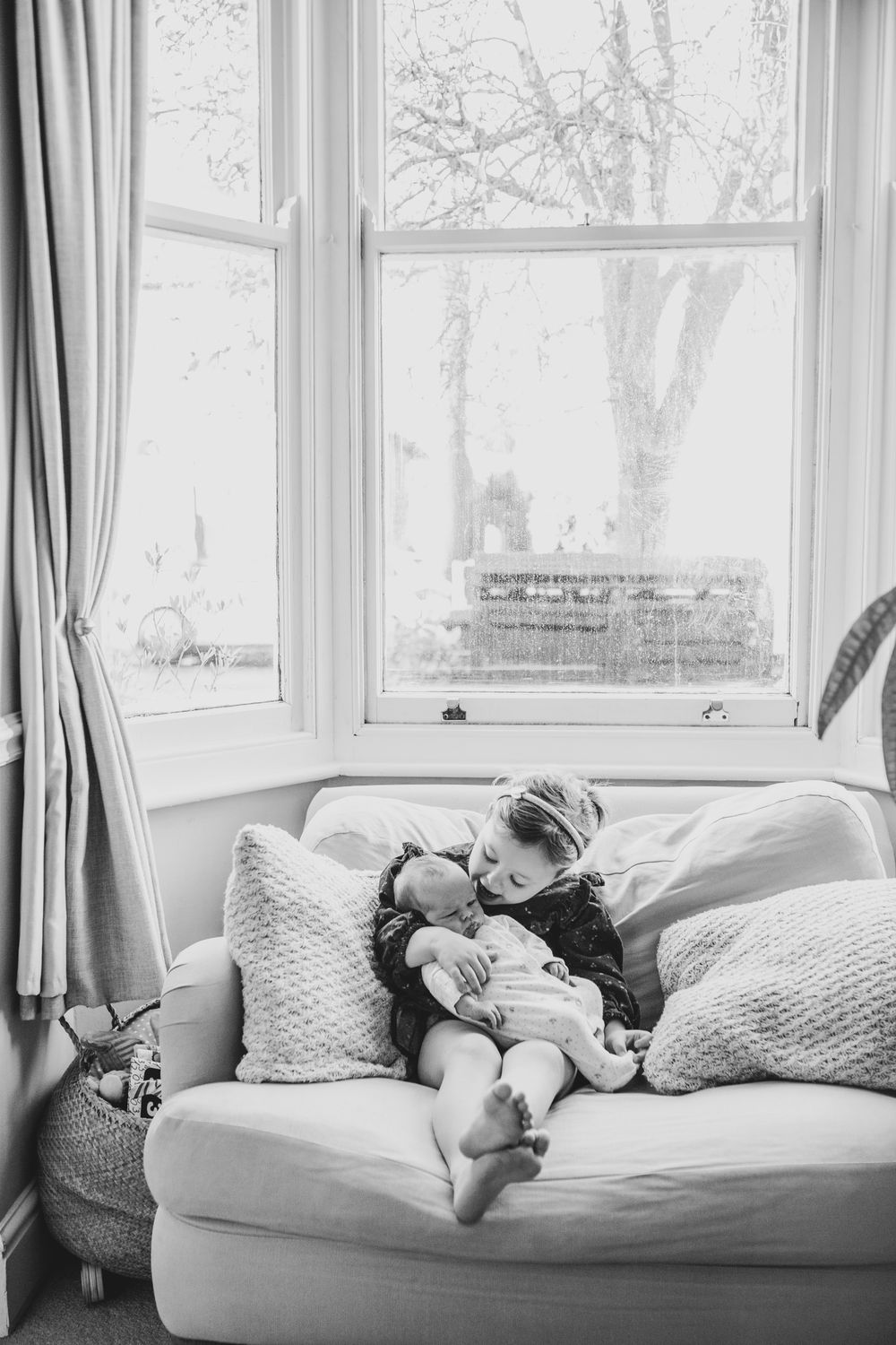 Black and white photo of someone napping peacefully on a couch beneath a bright window with curtains.