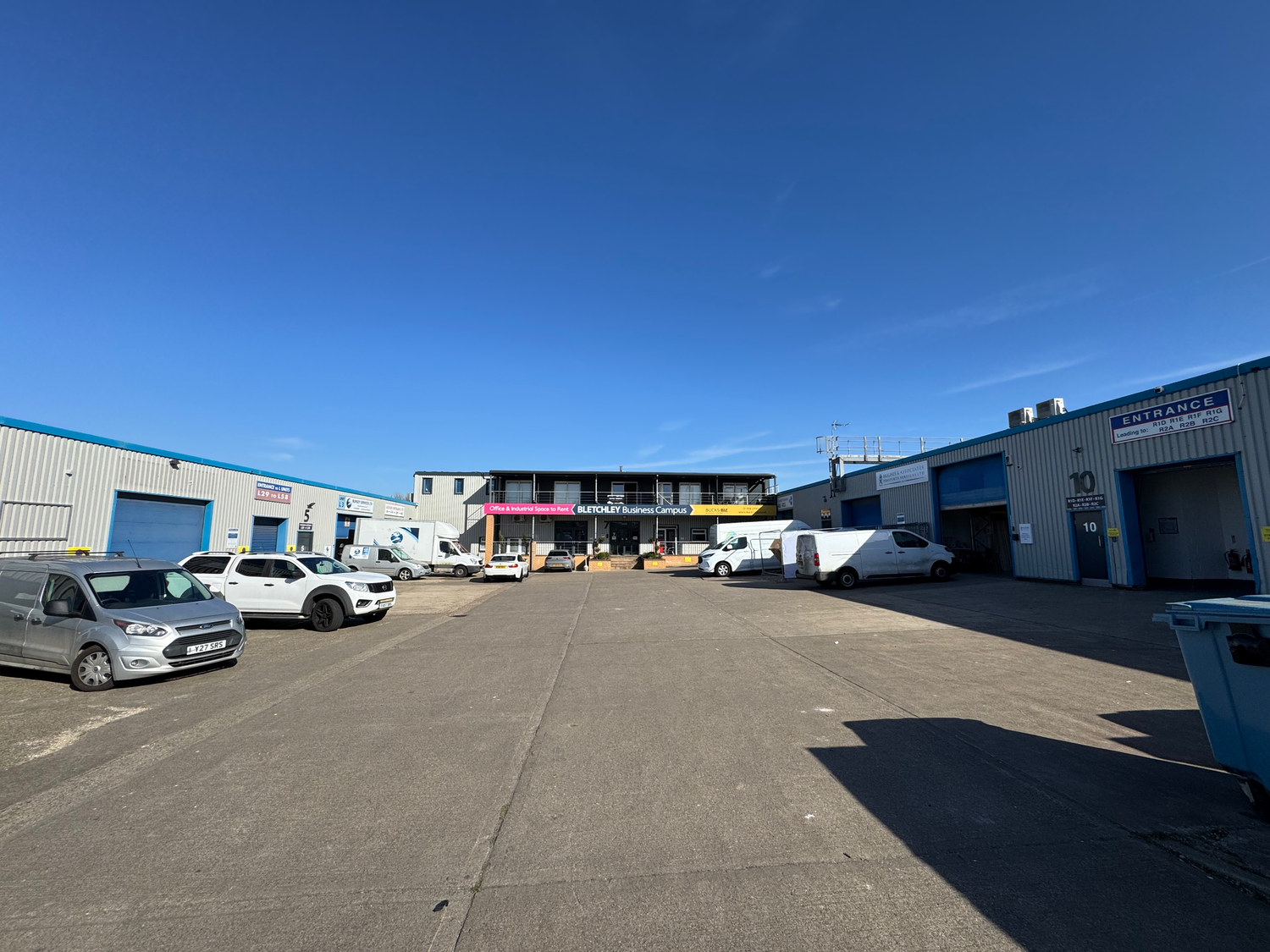 Industrial strip mall with parked cars and automotive service buildings under bright blue sky.