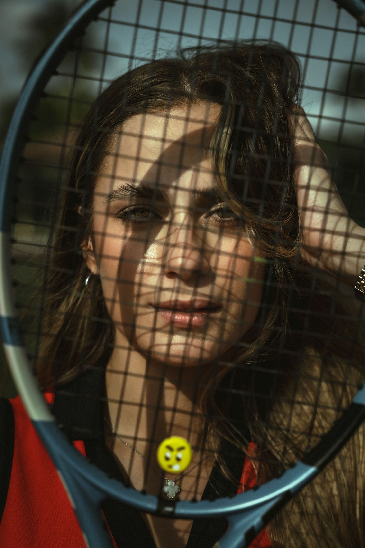 Tennis player poses behind racquet strings with creative mesh pattern lighting in an artistic portrait.