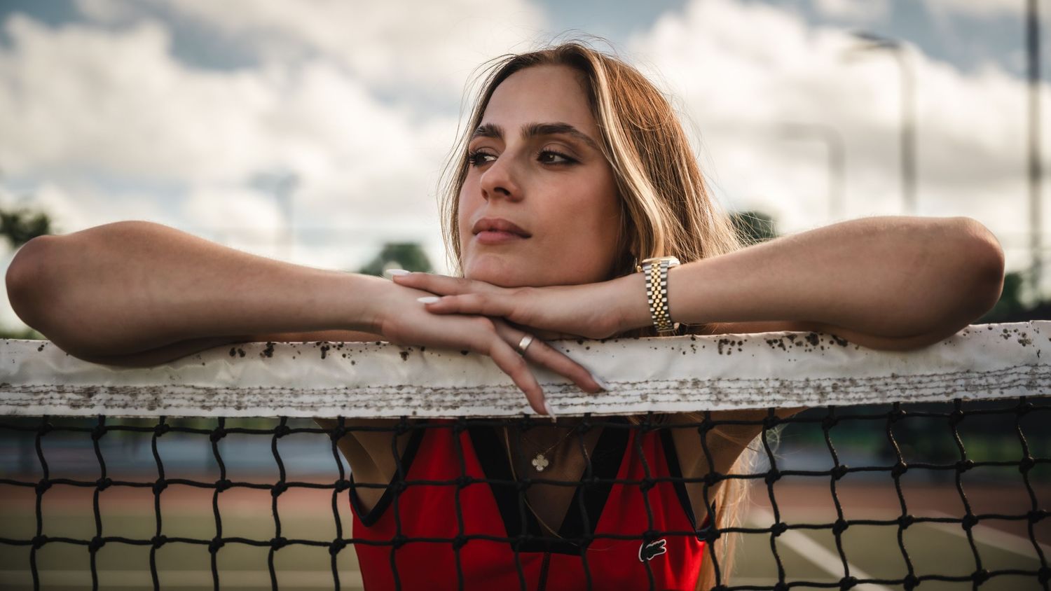 Athlete rests on tennis net during sunset with contemplative expression.