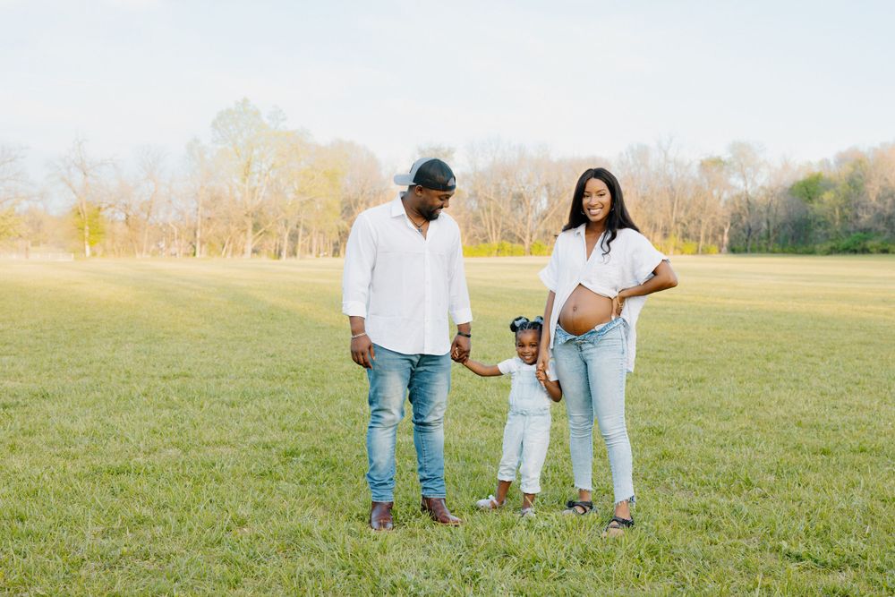 Family spending time together on a grassy field during autumn with fall foliage in the background.