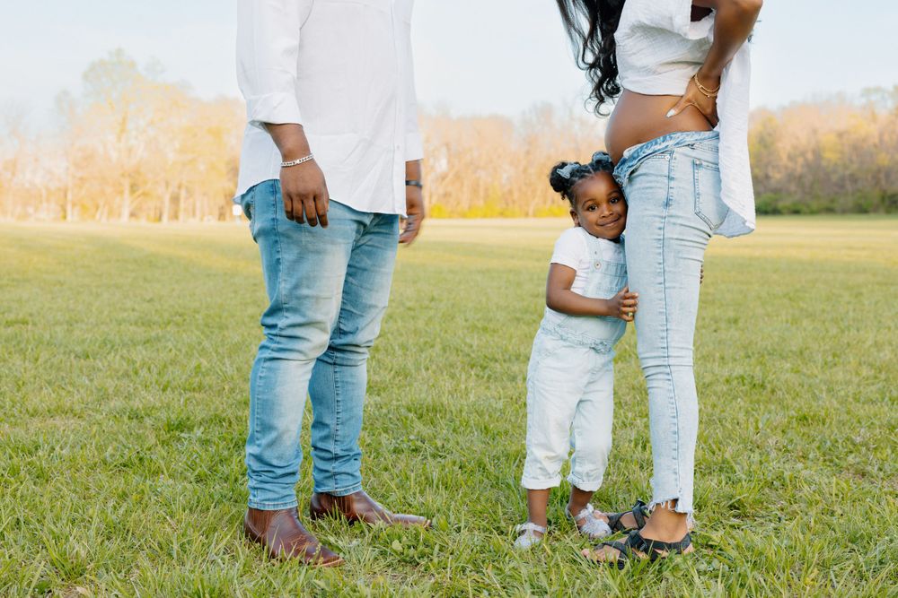 Family members wearing casual denim and white clothes stand together on a grassy field during golden hour.