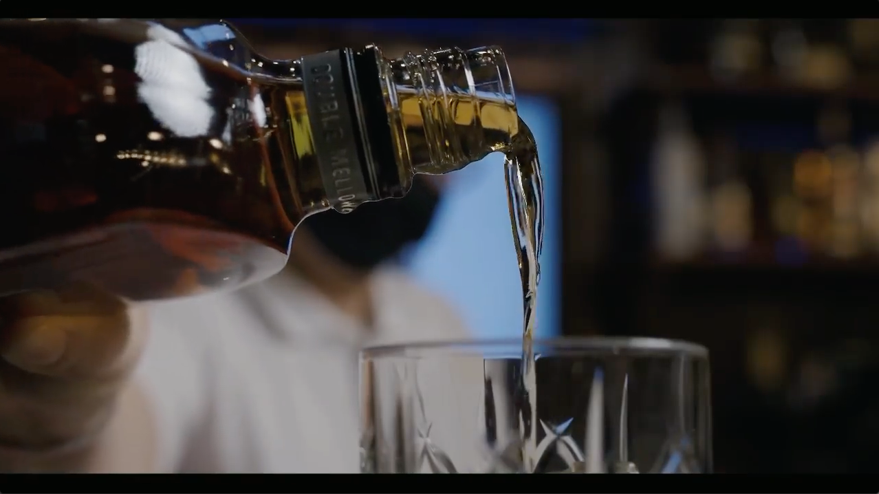 Dark liquid being poured from bottle into glass in dramatic lighting.
