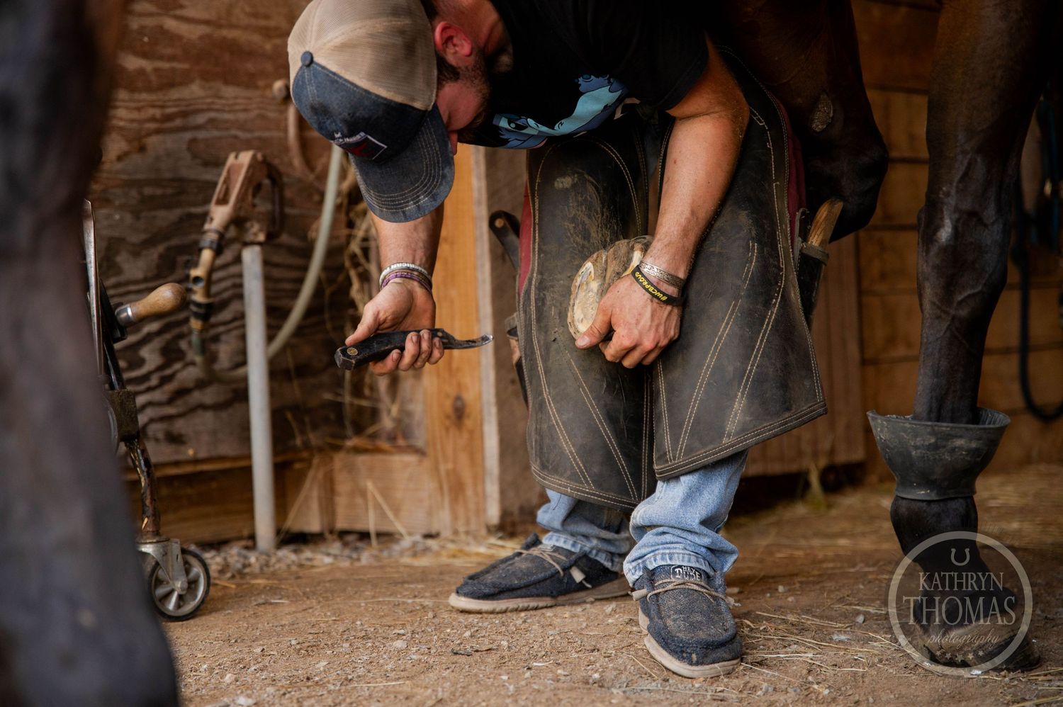 Close-up shot of a farrier working on a horse's hoof in a wooden stable.
