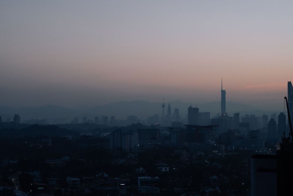 A misty cityscape silhouette during sunset with tall buildings and a prominent tower in the background.