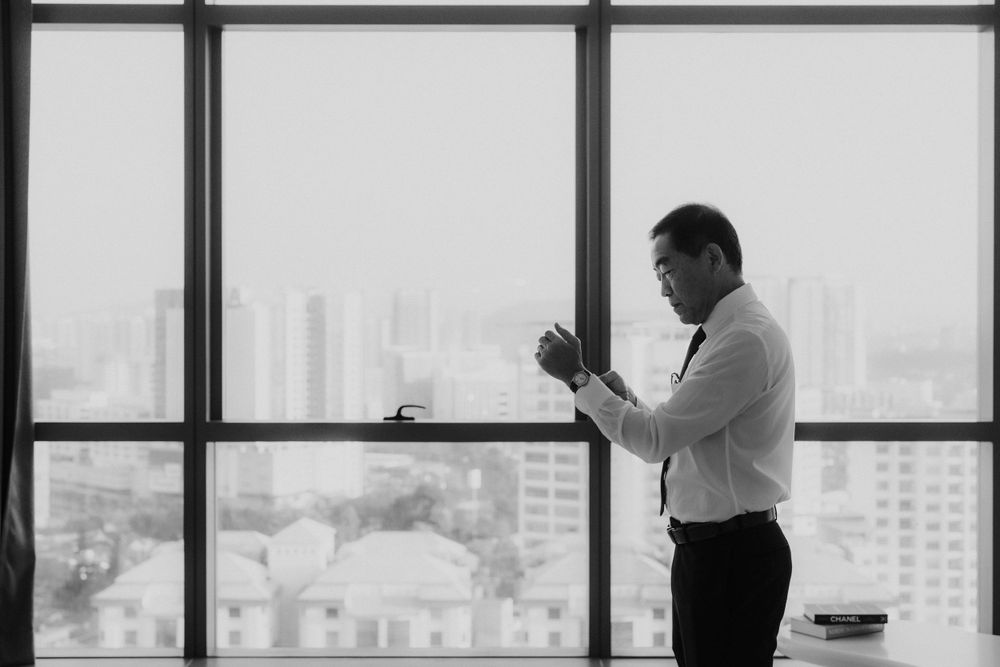 A businessman in formal attire stands silhouetted against large windows overlooking a city skyline.
