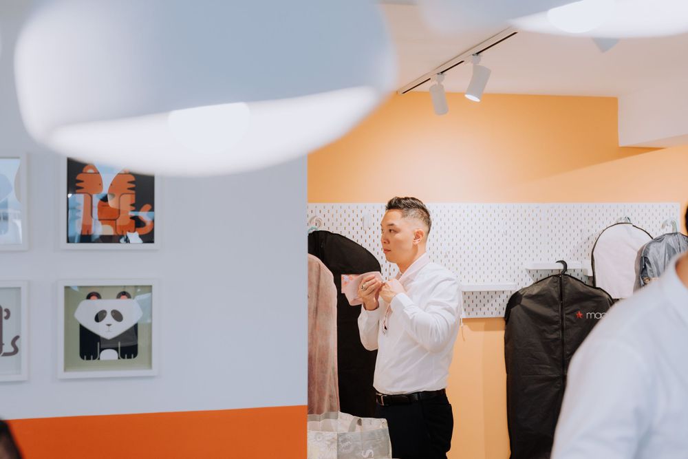 A person in a white dress shirt hangs formal attire in a dressing room with orange walls and framed artwork.