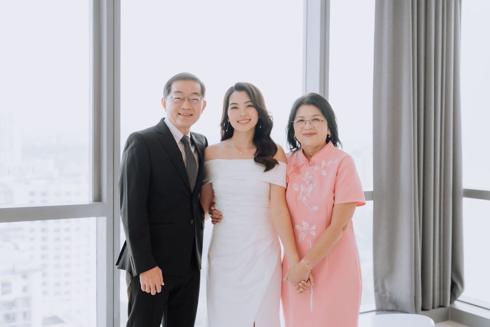 Three people in formal attire pose together by a bright window in a high-rise building.