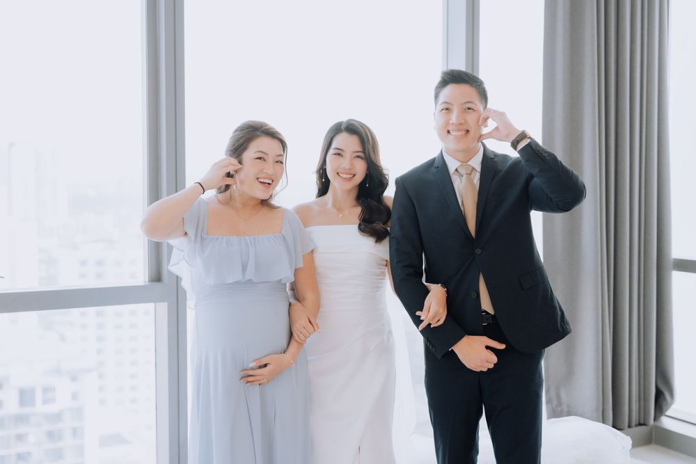Three wedding party members in formal attire laugh together by a bright window in a modern venue.