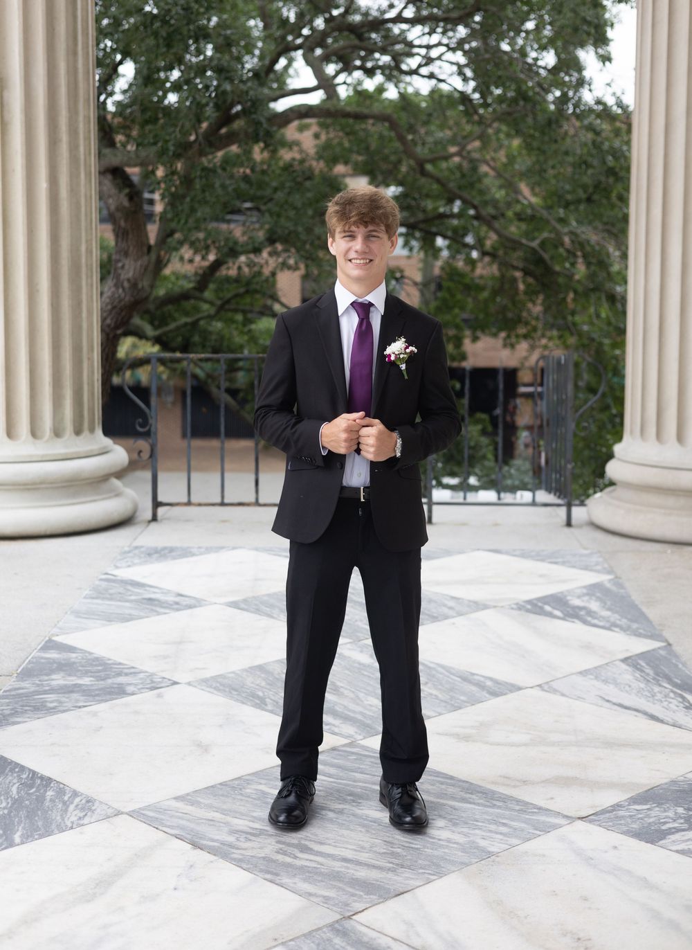A formal portrait showing someone in prom attire on a decorative tile floor between white columns.