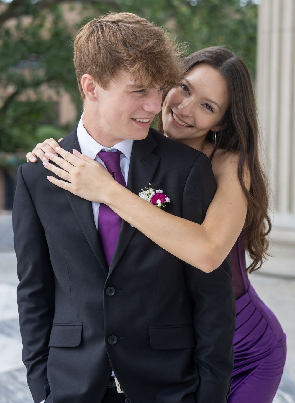A couple in formal attire embrace while wearing matching purple accents at a formal event.