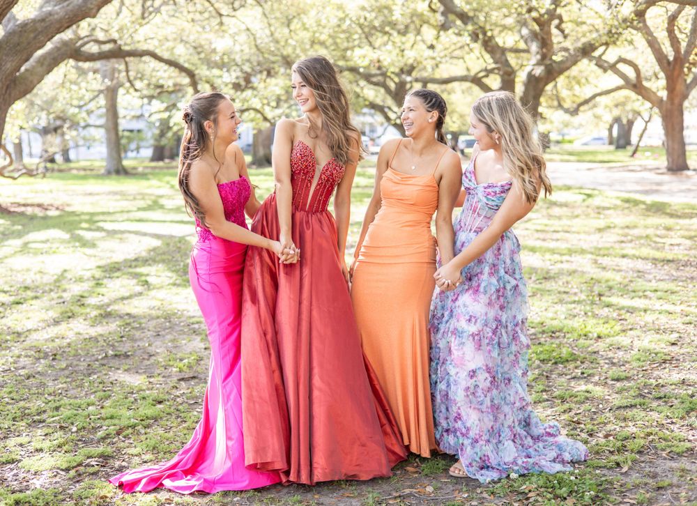 Four friends in elegant formal dresses pose together under oak trees draped with Spanish moss.