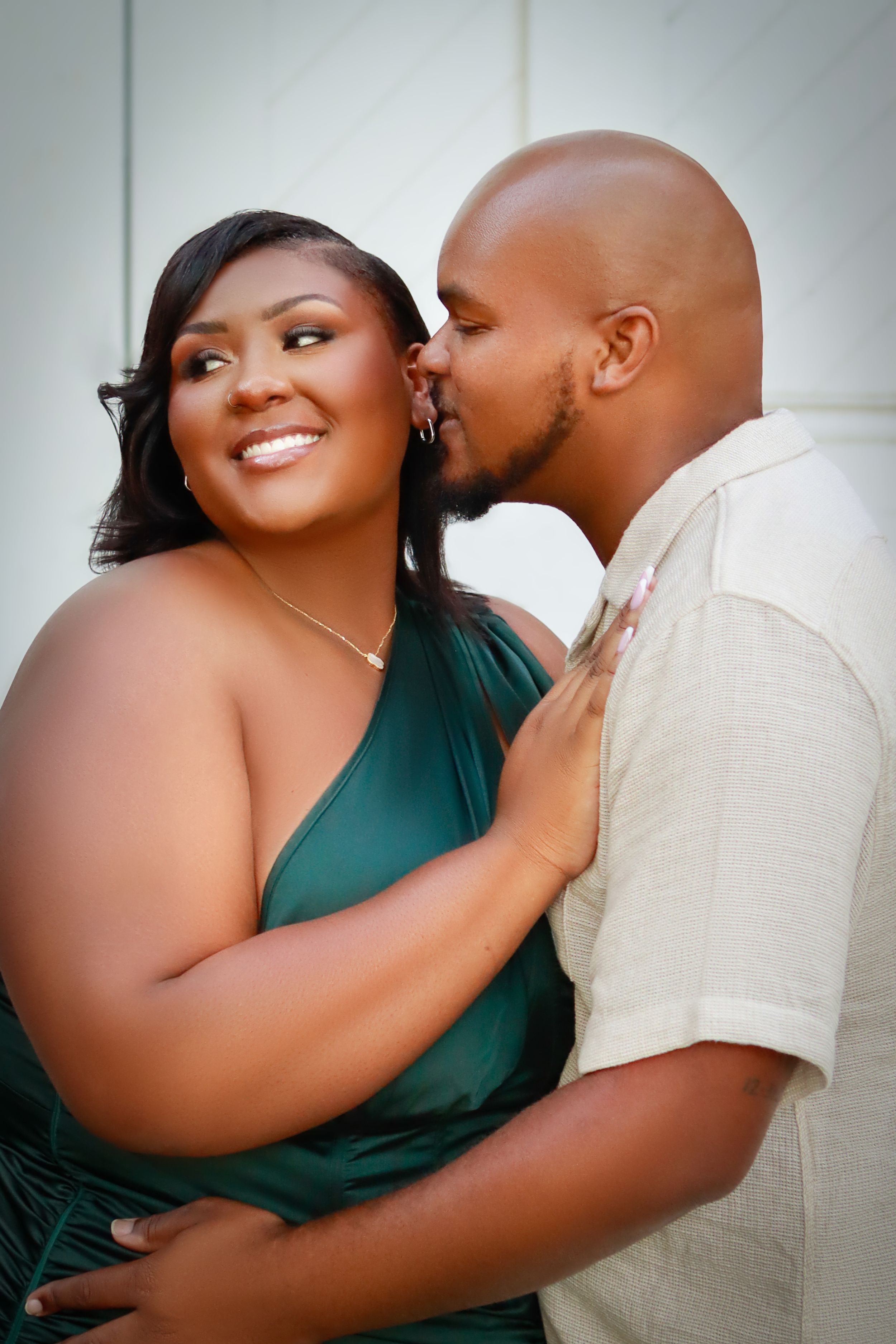 A romantic couple sharing an intimate moment, with one wearing an emerald green dress and the other in a cream shirt.