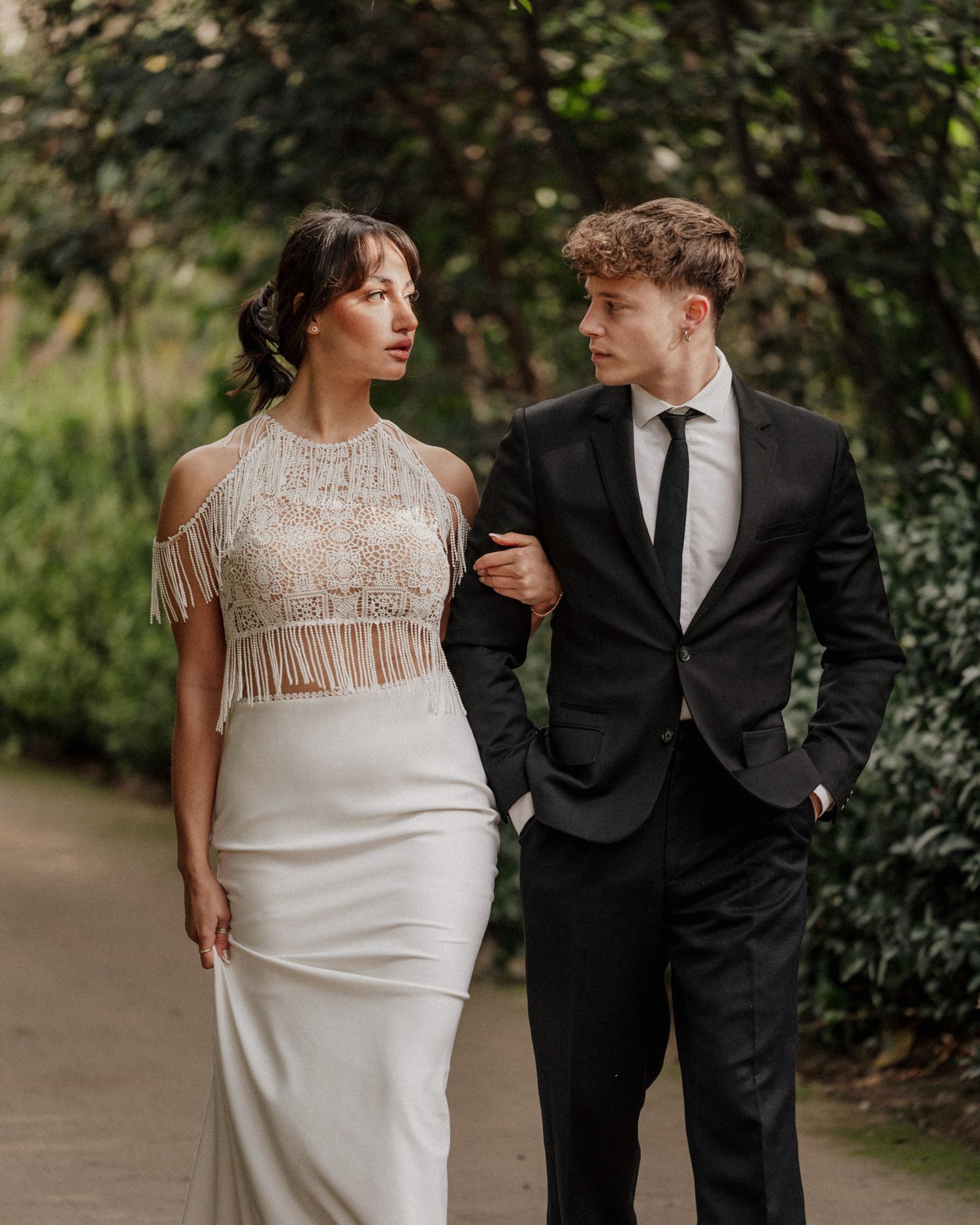 Elegant couple in formal attire posing together on a garden path.