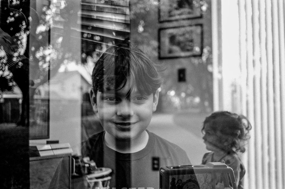 Black and white artistic double exposure photograph combining window reflections and street scenes in an urban setting.