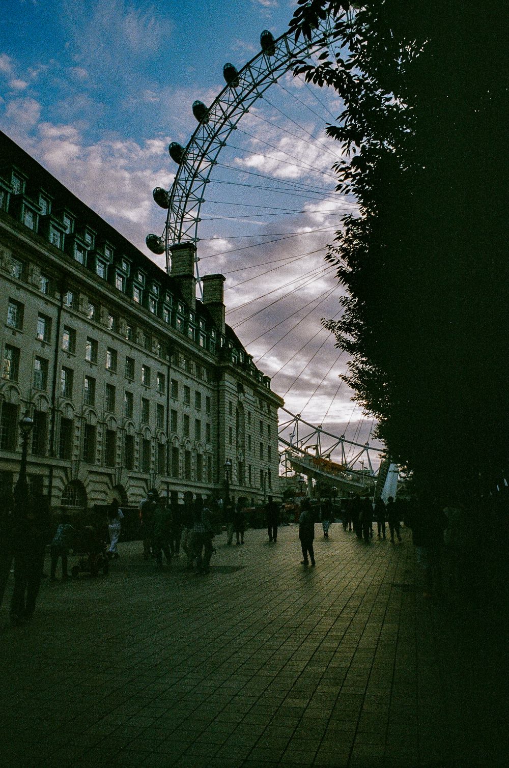 A moody silhouette of the London Eye Ferris wheel against a dramatic evening sky along the South Bank.