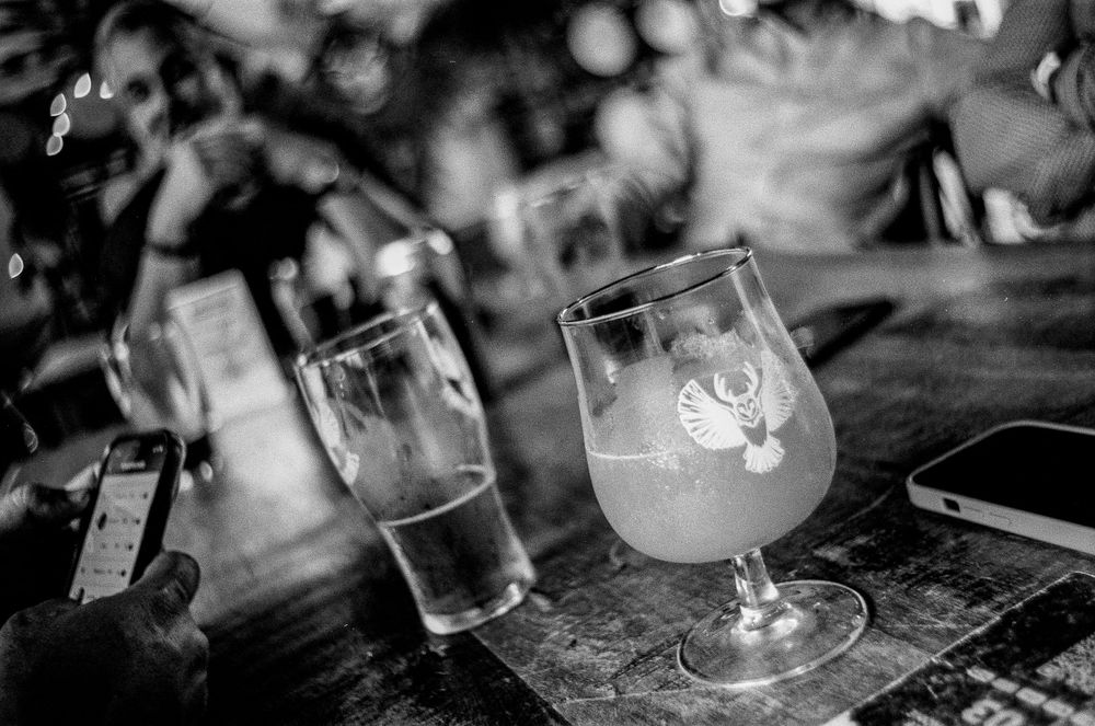Black and white photo of beer glasses on a wooden table in a bar setting with condensation and logo visible on glass.