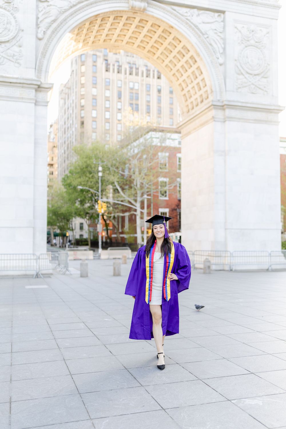 Graduate in purple academic regalia stands centered under historic stone arch.