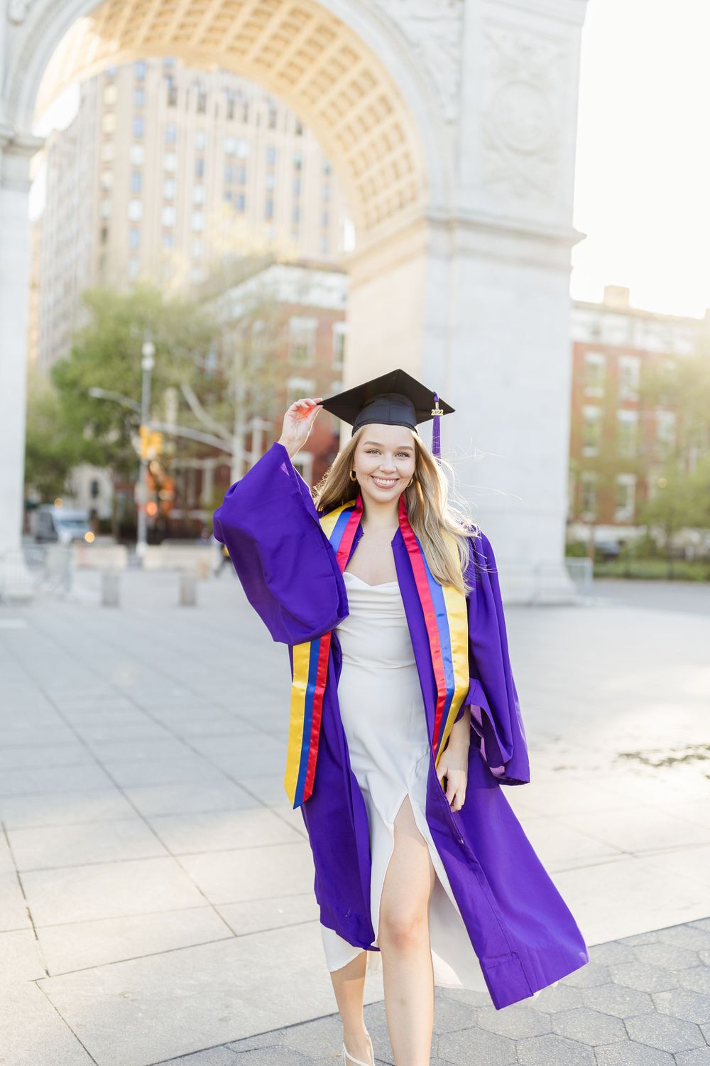 Graduate in purple regalia celebrating under historic Washington Square Arch.