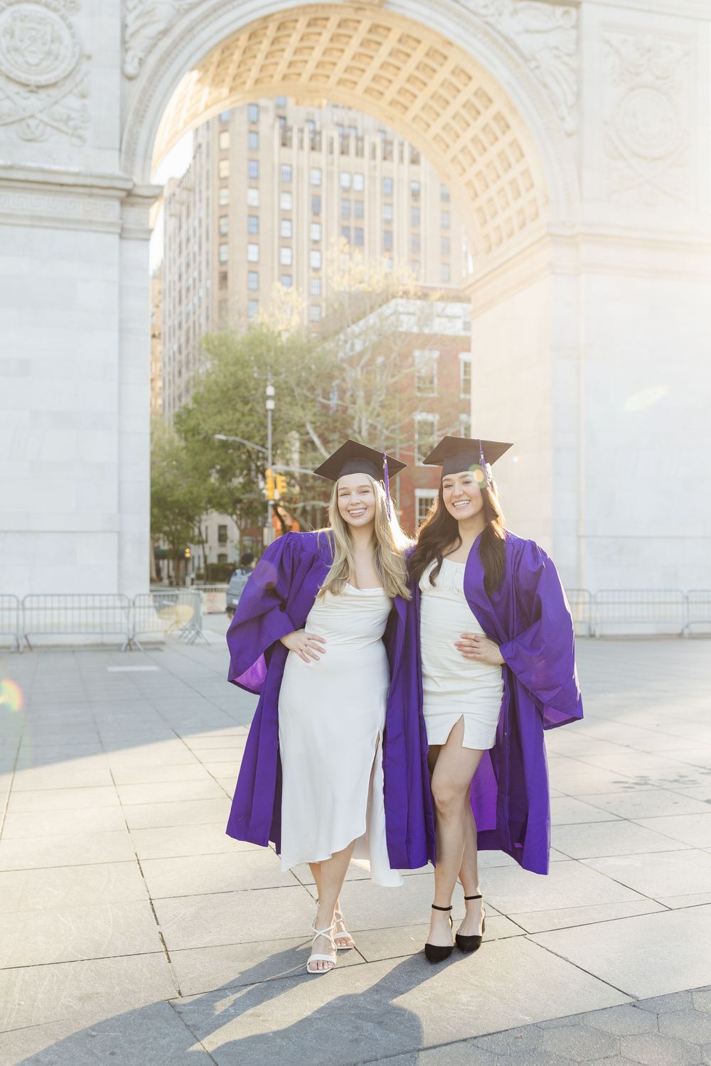 Two graduates in purple commencement robes posing at Washington Square Park.