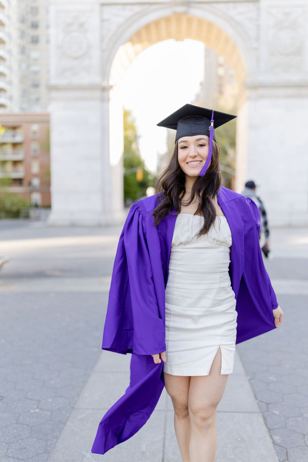 Graduate wearing purple graduation gown and cap standing under iconic stone arch.