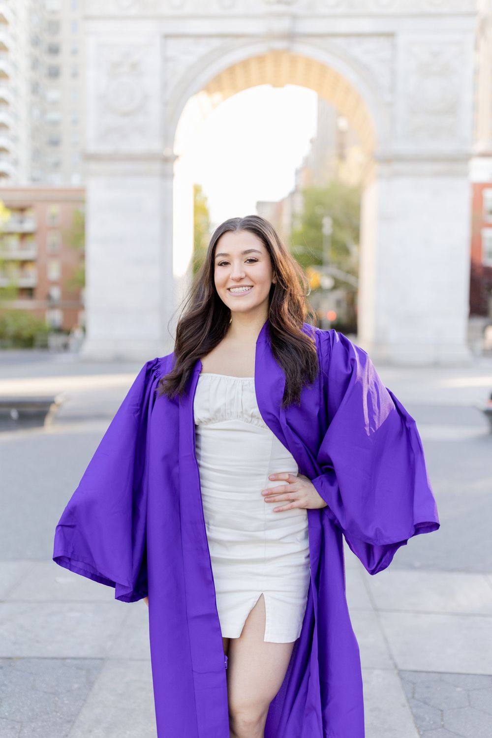 Graduate in bright purple commencement robe posing beneath Washington Square Arch.
