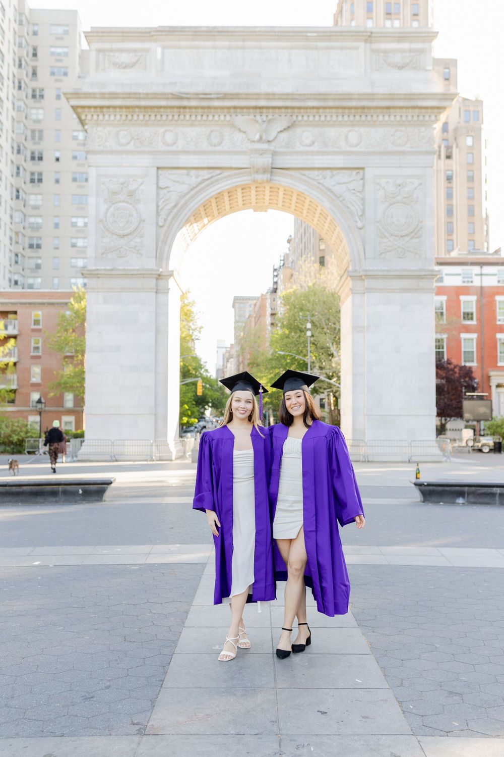 Two graduates pose in matching purple commencement gowns at Washington Square Arch.