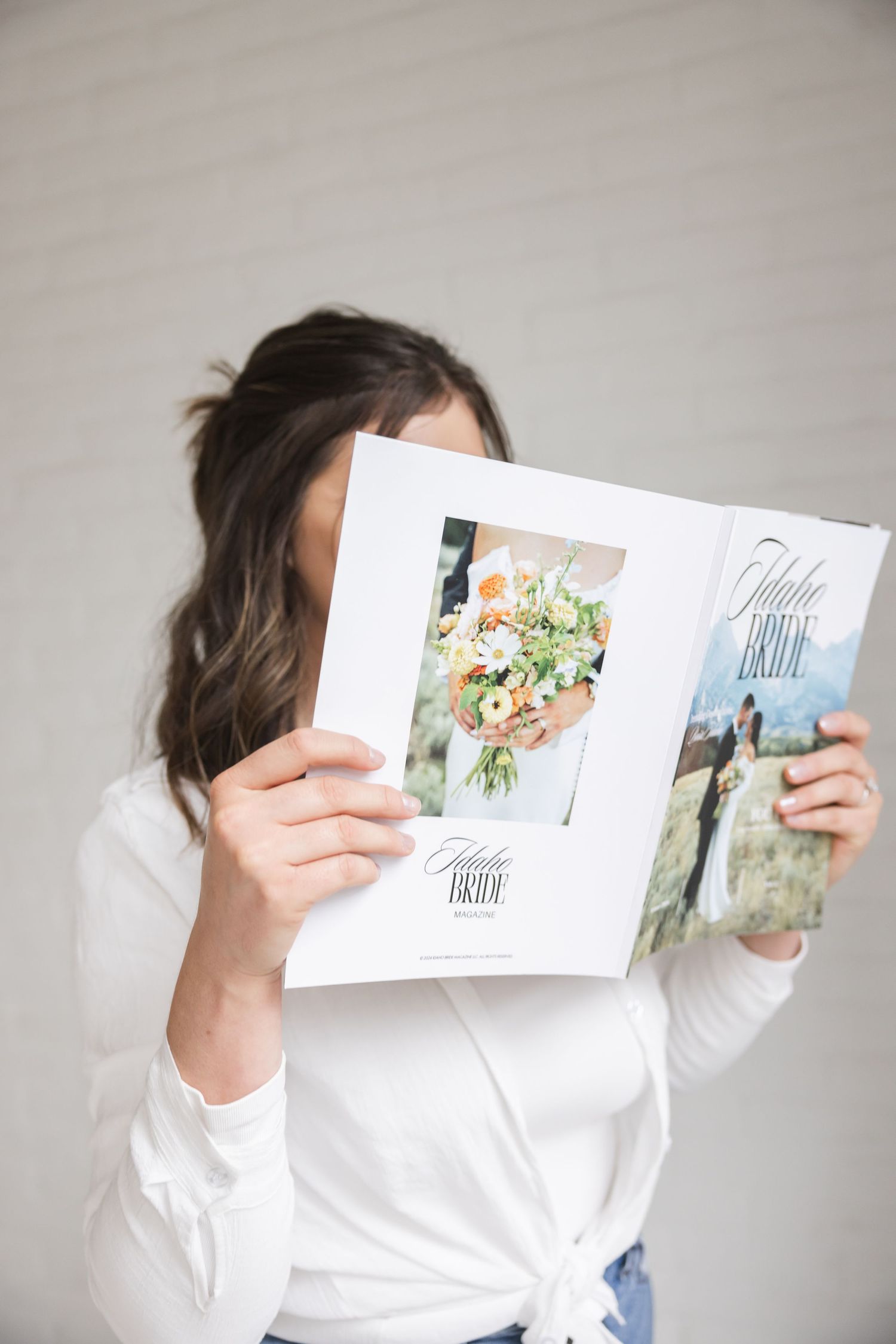 Someone in a white top holds up an open wedding photo album showing floral bouquet and couple photos.