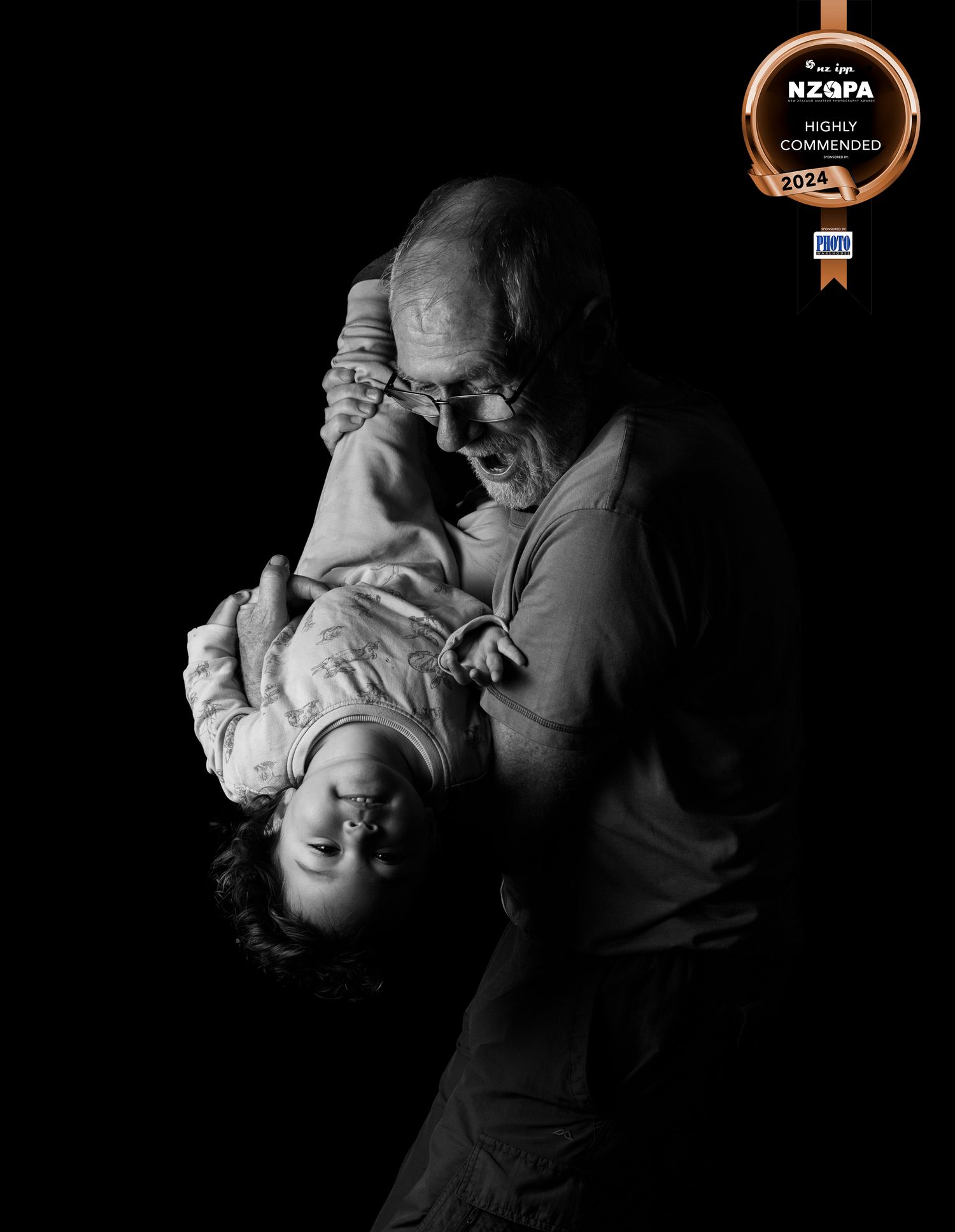 Emotive Black and white Image of a Grandfather playfully holding his young grand daughter upside down. CL Photography