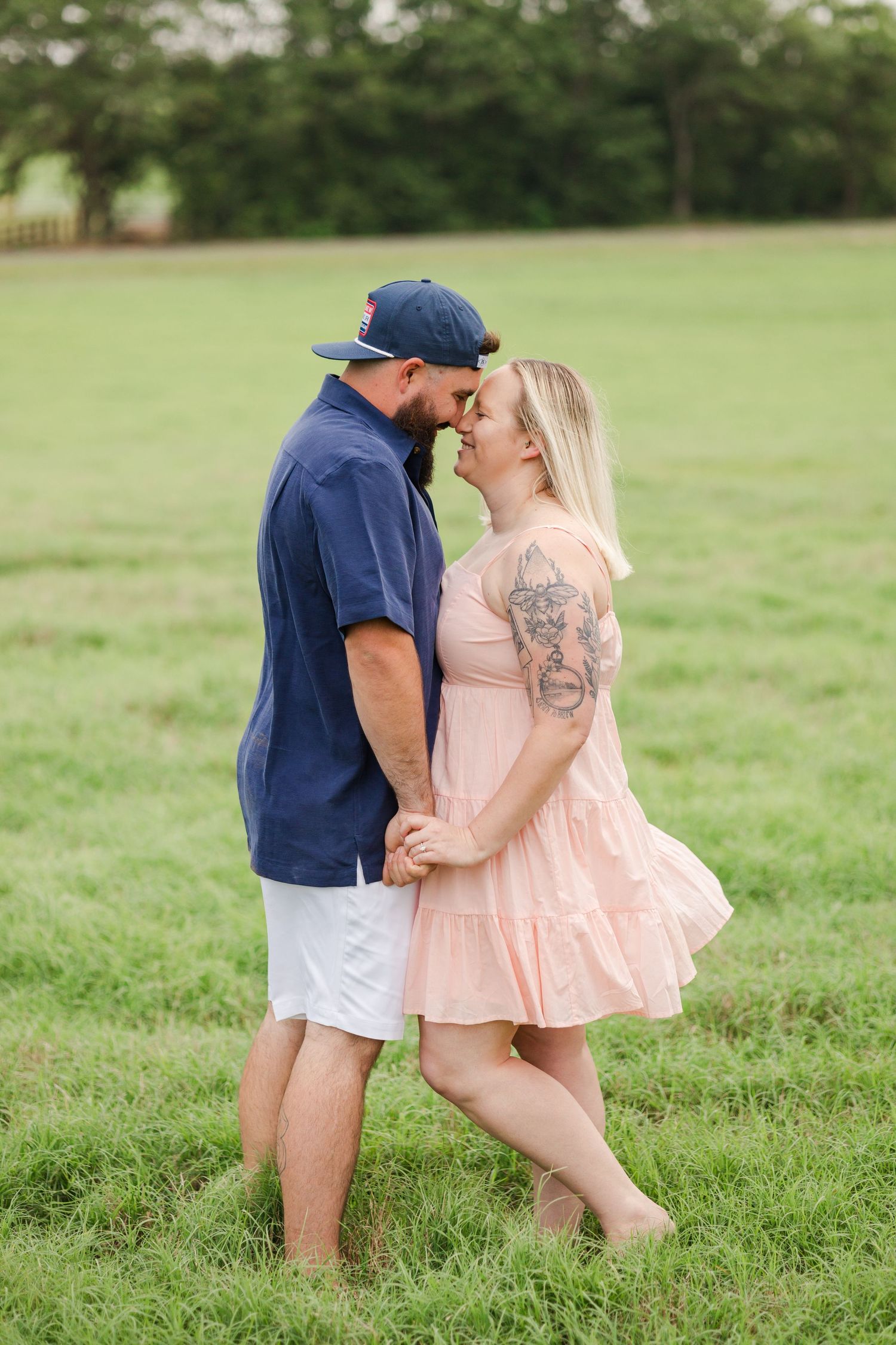 Romantic couple embracing in a grassy field, wearing navy and pink casual outfits.