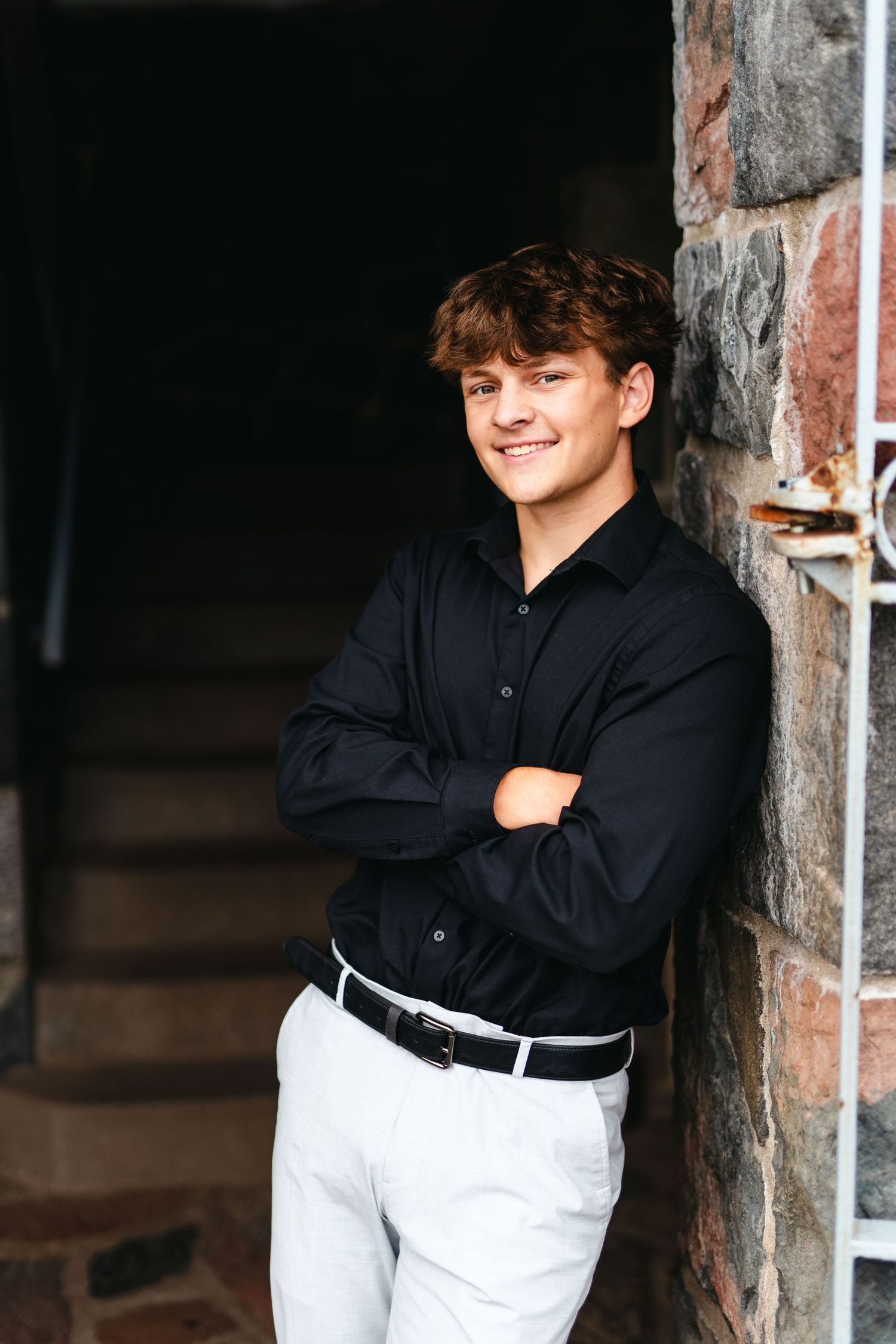 Young person in a navy button-down shirt and white pants poses confidently against a stone wall.